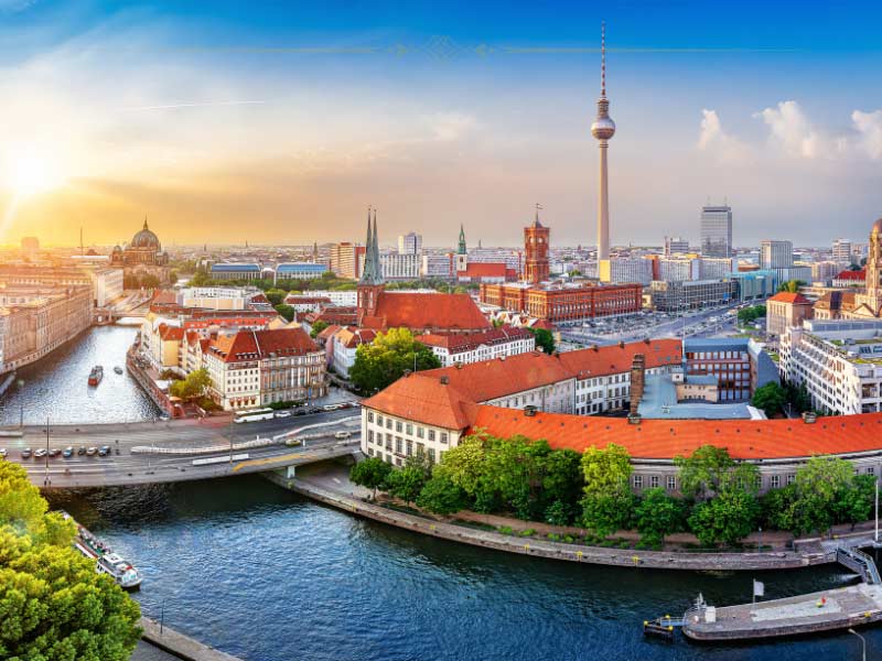 An aerial photo of Berlin, with the river in prim plan and small buildings with orange rooftops along it. You can see the Berlin Tower in the background.