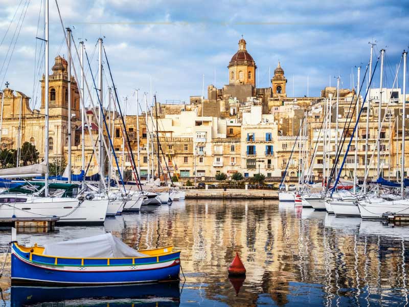 Old buildings reflecting in the water of the harbour in front, on which there are small boats anchored.