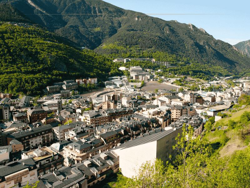 A view over the town of Andorra la Vella from above. The city is located in a valley, surrounded by mountains covered with thick forests.