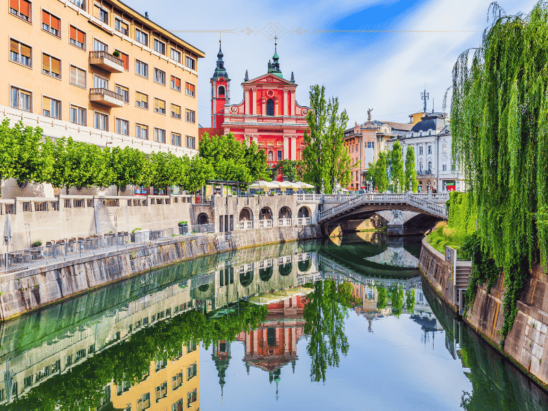 A view over the river towards the Dragon bridge and the pink-salmon coloured cathedral. The water is still and the city reflects in it.
